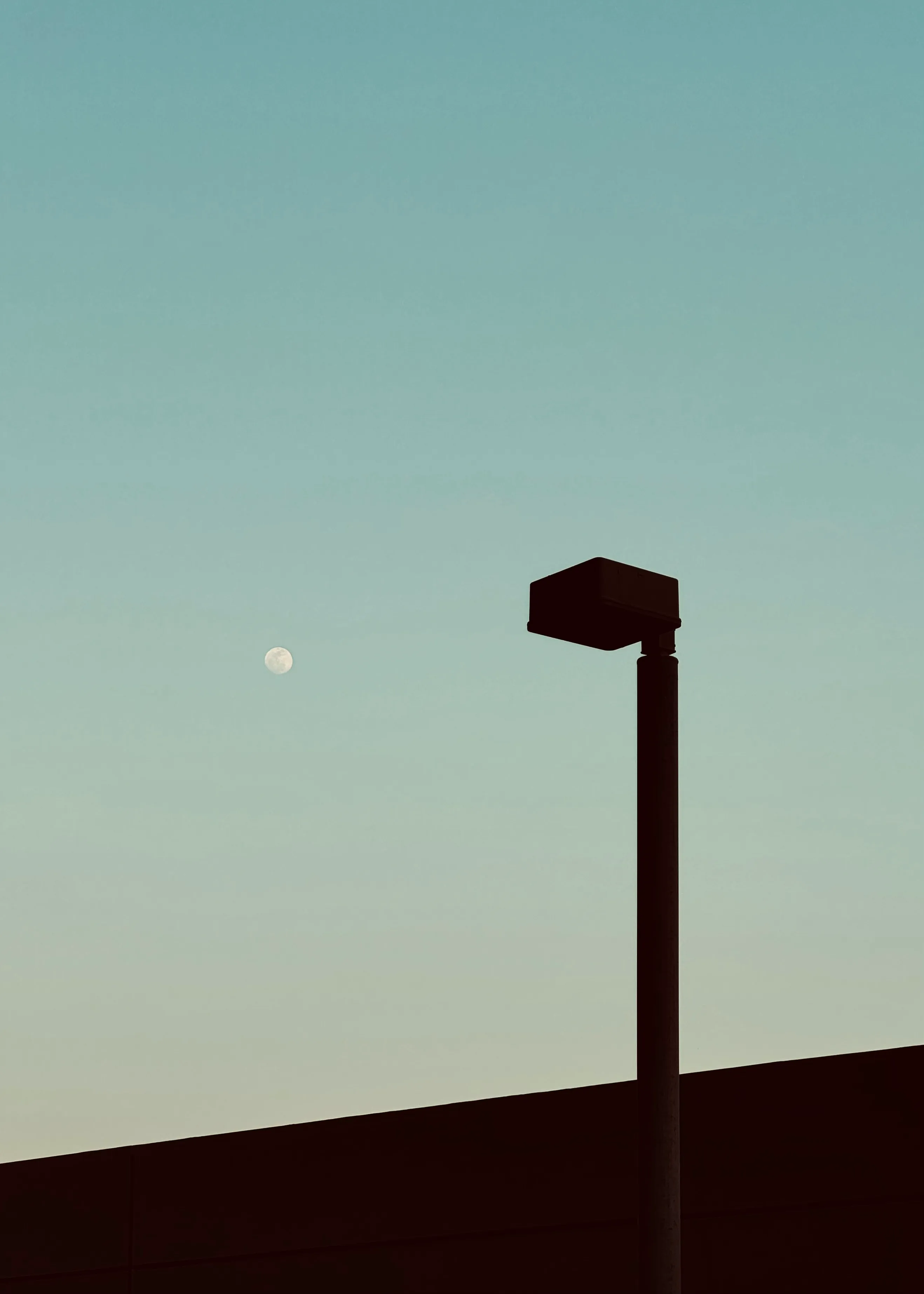 Lone car-park light and the moon in a dusk sky